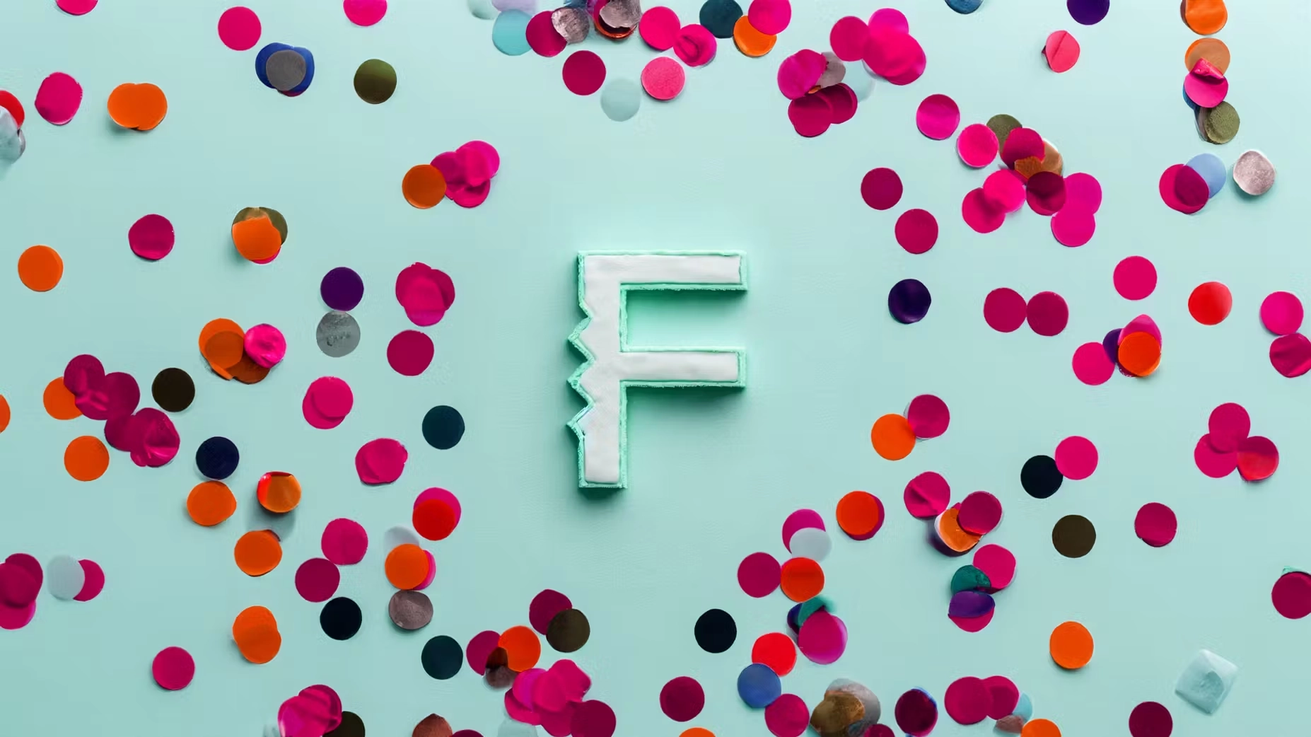 A cake in the shape of the Flux "F" logo sits on a green. surface, surrounded by confetti