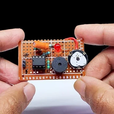 A prototype of an electronics project consisting of buzzer, a coin cell battery and looks like an 555 timer IC