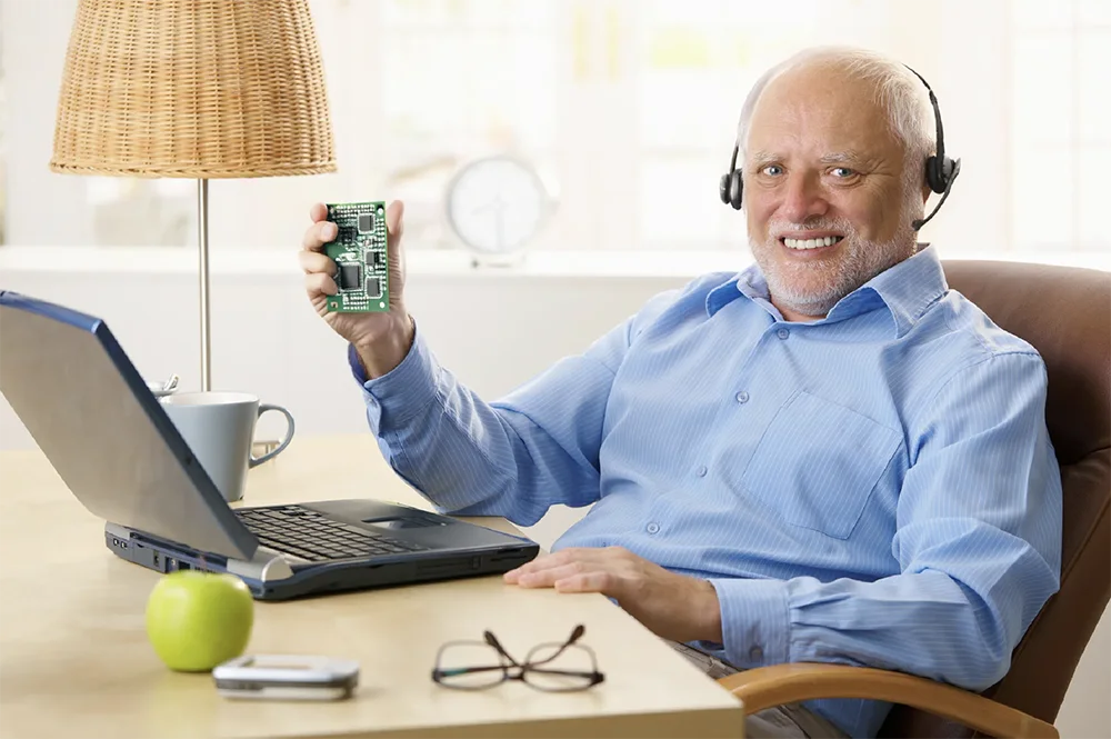 An old man holding a PCB board in front of his computer, suggesting he got a good customer service from using Flux, a PCB design tool